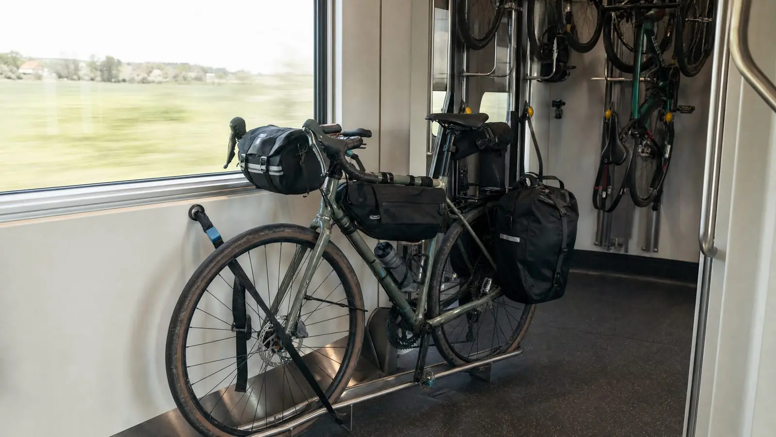 A loaded steel touring bicycle strapped upright in the bicycle compartment of a moving passenger train